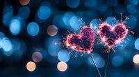 Pink sparkler hearts against blurred blue bokeh background create romantic mood. Glowing heart shapes made with burning sparklers capture celebration and love.