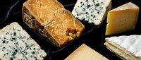 Gourmet cheese selection with blue cheese, aged cheddar and soft varieties arranged on dark slate board for culinary photography and food styling.