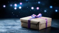 Gift box wrapped in kraft paper with sparkly purple ribbon on dark background with magical glowing bokeh lights creating festive holiday atmosphere.