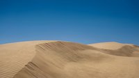 Sand dunes with rippled texture under clear blue sky in arid desert landscape for travel and nature backgrounds.