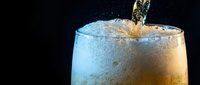 Refreshing cold beverage being poured into frosted glass with ice cubes and bubbles against dark background for summer drinks and cocktail concepts.