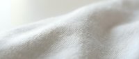 Soft white cotton fabric texture with natural folds and wrinkles. Close-up macro shot showing detailed weave pattern for textile and fashion design projects.