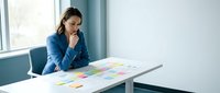 Young Asian businesswoman in blue blazer analyzing colorful sticky notes on desk in modern office, planning strategy and organizing workflow.