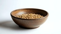 Raw soybeans in rustic brown ceramic bowl on white background, natural lighting creates soft shadows highlighting organic texture and wholesome ingredients.
