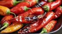 Fresh red and orange chili peppers with glossy surface and green stems arranged on dark plate, macro food photography showing texture and natural shine.