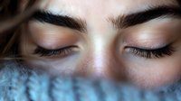 Close up portrait of young woman with closed eyes, long eyelashes and well-groomed eyebrows against blurred blue background. Macro beauty shot showing natural makeup look.