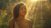 Young African American woman with natural curly hair in golden sunlight surrounded by wildflowers, eyes closed in peaceful expression during sunset, wearing tank top.