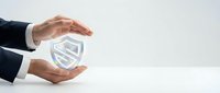Male professional in dark business suit protecting glowing shield icon with both hands against white background, representing cybersecurity, data protection, and risk management solutions.