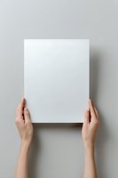 Female hands holding blank white paper sheet against neutral gray background, mockup for presentation or design placement.