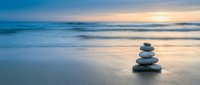 Zen stone stack on peaceful beach at sunset with soft waves and golden light reflecting on wet sand creating tranquil meditation atmosphere.
