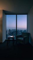 Modern high-rise apartment interior with floor-to-ceiling windows overlooking sprawling cityscape at twilight. Dark armchair and small table create intimate seating area for relaxation and contemplation.