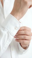 Man buttoning white dress shirt cuff, close-up of hands fastening pearl button, formal business style concept for fashion and lifestyle.