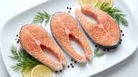 Fresh salmon steaks on white plate with dill and lemon garnish. Raw fish fillets ready for cooking, grilling or baking in kitchen preparation.