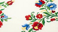 Traditional folk embroidery with colorful floral motifs on cream fabric. Red and blue flowers with green leaves create decorative border pattern for textile design.