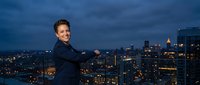 Professional businesswoman with crossed arms smiling confidently against illuminated city skyline at dusk for corporate success and leadership concepts.
