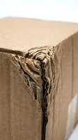 Damaged brown cardboard box with torn corner showing wear and shipping damage on white background for packaging and delivery concepts.
