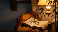 Cozy reading nook with open book, eyeglasses and warm lamp light creating peaceful evening atmosphere for relaxation and study.