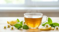 Herbal chamomile tea in glass cup with fresh mint leaves and lemon slice on wooden table near window for relaxation and wellness.