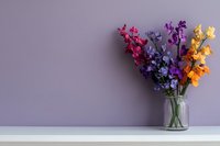 Colorful snapdragon flowers in glass vase on white shelf against purple wall background, creating minimalist floral composition with copy space for text.