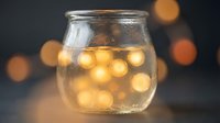 Whiskey or bourbon with ice cubes in clear glass jar against blurred warm bokeh background, suitable for beverage, alcohol, and lifestyle advertising.