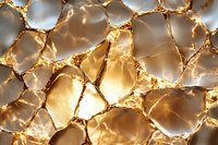 Golden cracked surface with light shining through translucent fragments creating abstract pattern of illuminated geometric shapes and shadows.
