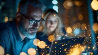 Mature Caucasian businessman with gray beard and glasses working late at office, illuminated by laptop screen with magical bokeh light effects and glowing particles.