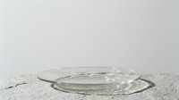 Empty glass plate on sandy surface with neutral background, suitable for product placement and design mockups.
