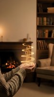 Hand holding glowing golden spiral light trail in cozy living room with fireplace and bookshelf creating magical atmosphere for holiday decorating concepts.