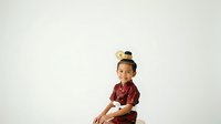 Young Asian male child wearing burgundy plaid shirt and decorative top hat with gold accents, seated against white background for portrait use.