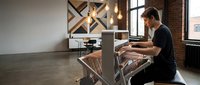 Young professional man working on laptop in modern industrial office space with exposed brick walls and pendant lighting for business productivity.