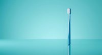 Blue toothbrush standing upright on turquoise background with soft lighting and minimalist composition for dental hygiene and oral care concepts.
