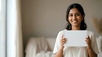 Young South Asian woman with long dark hair smiling while holding blank white card, wearing cream colored shirt, suitable for business, marketing, testimonial and corporate communication projects.