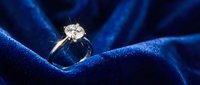 Elegant diamond engagement ring with sparkling solitaire stone on luxurious blue silk fabric background for wedding and jewelry concepts.