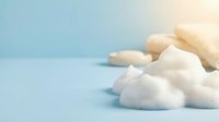 Fluffy white foam cleanser with soap bars on a soft blue background, copy space for skincare and beauty product advertising.