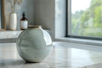 Elegant spherical ceramic vase in soft sage green placed on marble countertop near window, perfect for modern minimalist interior design and home decoration styling.