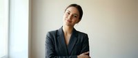 Confident professional businesswoman in dark suit with crossed arms smiling in modern office interior for corporate leadership and success concepts.