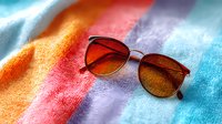 Stylish sunglasses with orange gradient lenses on colorful pastel textile background with soft shadows and light effects, fashion accessory photography.