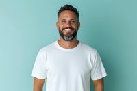 Confident mature Caucasian man with beard and trendy haircut wearing white t-shirt smiling at camera against turquoise background. Lifestyle portrait for advertising.