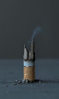 Burning cigarette with miniature city skyline emerging from filter, conceptual art about urban pollution and smoking dangers with rising smoke.
