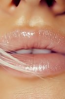Close-up of glossy pink lips with shimmering lip gloss and delicate string creating artistic effect, suitable for beauty and cosmetic advertising campaigns.