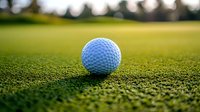 White golf ball on green grass course with soft bokeh background and natural lighting, close-up macro shot showing ball texture and dimples on putting green.