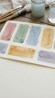 Watercolor paint palette with colorful brush strokes on paper, art supplies and brushes on wooden table for creative painting projects.