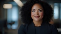 Young African American businesswoman with natural curly hair and confident smile wearing black blazer in modern office setting, representing professional leadership.