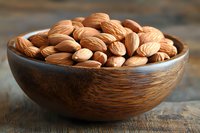 Fresh whole almonds in rustic wooden bowl on dark wooden table background, natural healthy snack food photography with soft lighting and shallow depth.