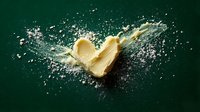 Fresh butter stick splashing into water with dynamic droplets and spray against dark green background for culinary and cooking concepts.