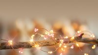 Warm glowing fairy lights with copper wire creating cozy ambient lighting on wooden surface for holiday decorating and festive atmosphere.