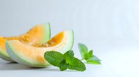 Fresh cantaloupe melon slices with bright orange flesh and green rind, garnished with mint leaves on white background, perfect for food marketing.