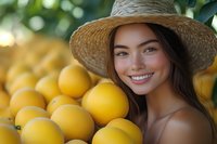Young Asian woman in straw hat smiling brightly near fresh yellow lemons at farmers market, natural summer lighting and bokeh background creates warm atmosphere.