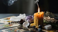 Burning beeswax candle with smoke surrounded by tarot cards, crystals, sage bundle and mystical objects for spiritual divination practices.