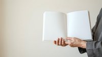 Mature man in business suit holding open blank white notebook with empty pages for mockup or branding purposes.